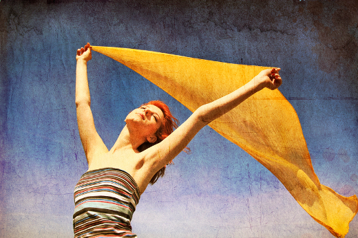 Young woman with open arms keep yellow silk on wind.